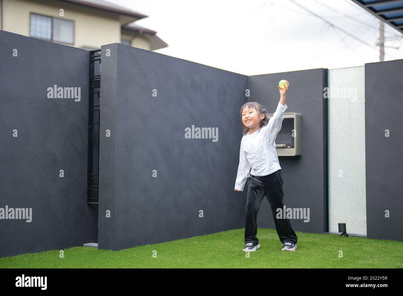 Un parent japonais et un enfant, un homme dans la vingtaine et une fille de 6 ans, jouent en se jetant des balles en plastique vert l'un sur l'autre dans le jardin clôturé de Banque D'Images