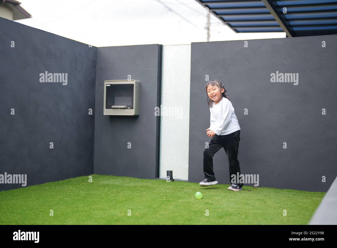 Un parent japonais et un enfant, un homme dans la vingtaine et une fille de 6 ans, jouent en se jetant des balles en plastique vert l'un sur l'autre dans le jardin clôturé de Banque D'Images