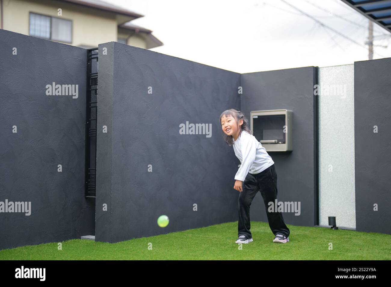 Un parent japonais et un enfant, un homme dans la vingtaine et une fille de 6 ans, jouent en se jetant des balles en plastique vert l'un sur l'autre dans le jardin clôturé de Banque D'Images