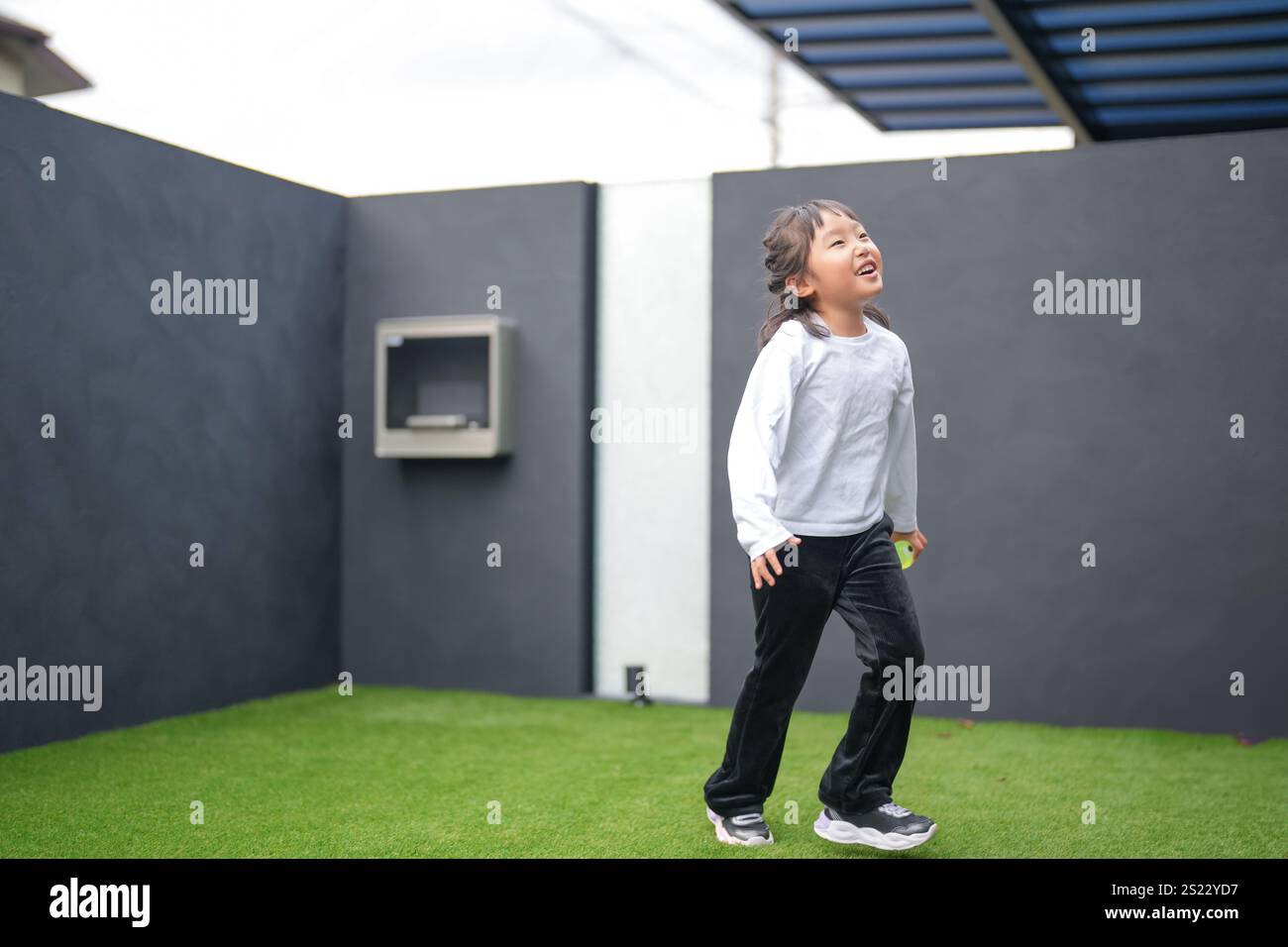 Un parent japonais et un enfant, un homme dans la vingtaine et une fille de 6 ans, jouent en se jetant des balles en plastique vert l'un sur l'autre dans le jardin clôturé de Banque D'Images