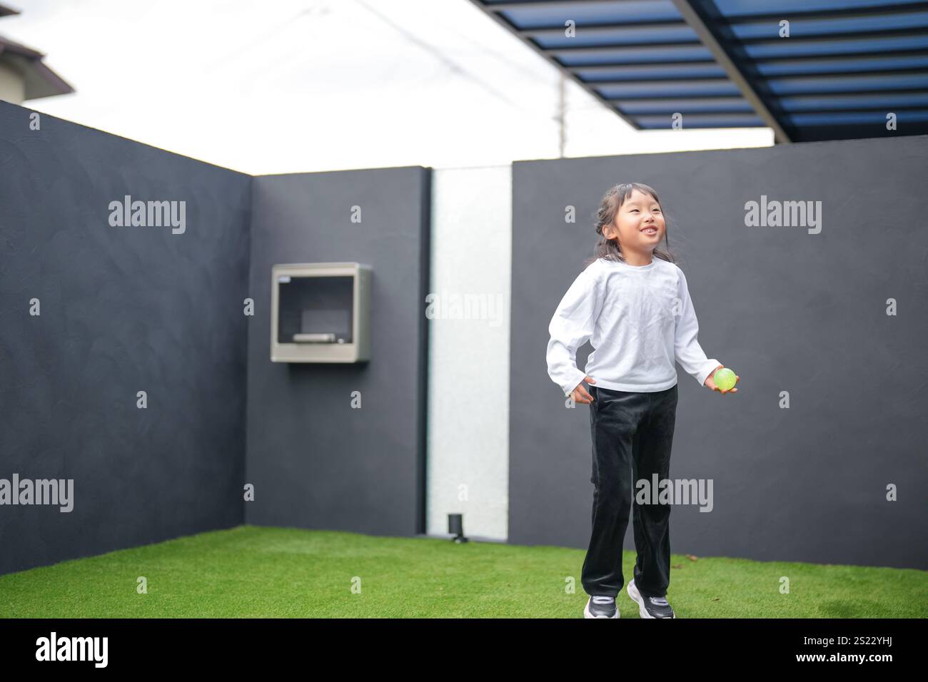 Un parent japonais et un enfant, un homme dans la vingtaine et une fille de 6 ans, jouent en se jetant des balles en plastique vert l'un sur l'autre dans le jardin clôturé de Banque D'Images
