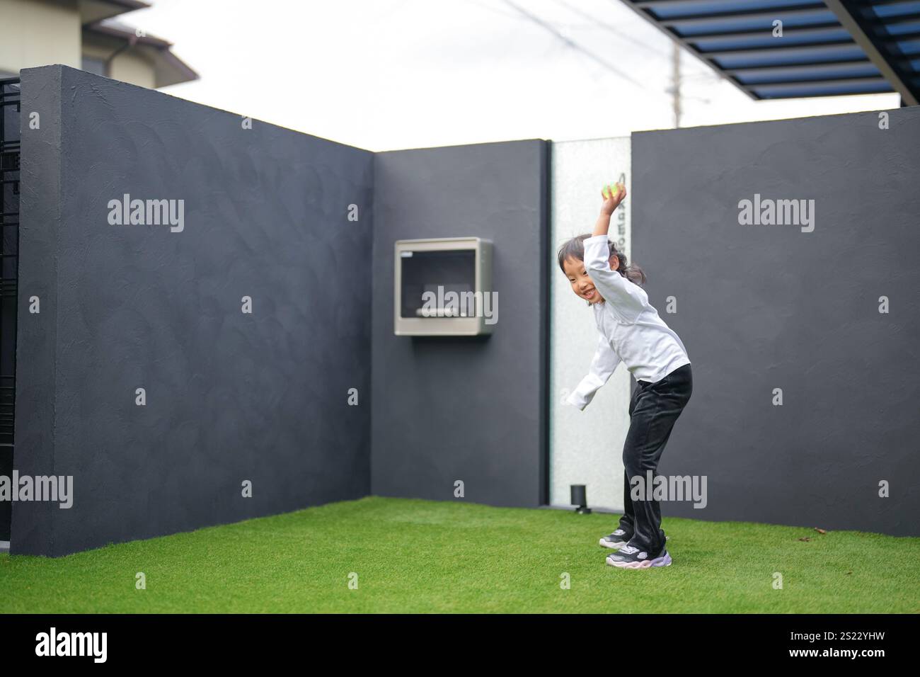 Un parent japonais et un enfant, un homme dans la vingtaine et une fille de 6 ans, jouent en se jetant des balles en plastique vert l'un sur l'autre dans le jardin clôturé de Banque D'Images