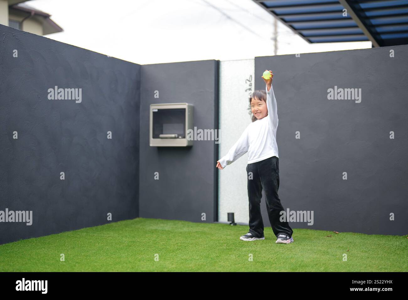Un parent japonais et un enfant, un homme dans la vingtaine et une fille de 6 ans, jouent en se jetant des balles en plastique vert l'un sur l'autre dans le jardin clôturé de Banque D'Images