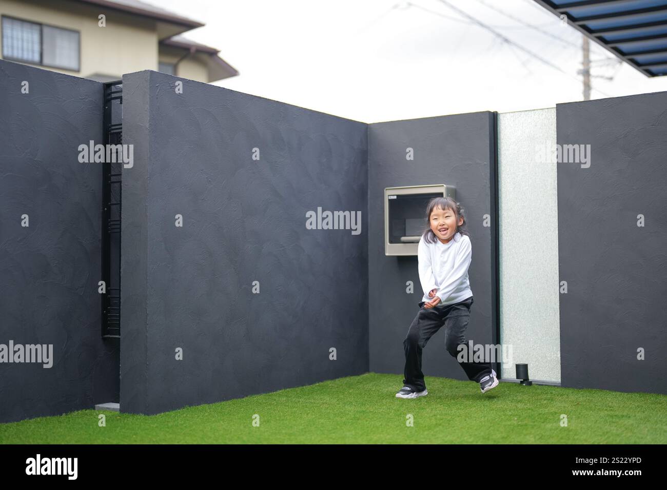 Un parent japonais et un enfant, un homme dans la vingtaine et une fille de 6 ans, jouent en se jetant des balles en plastique vert l'un sur l'autre dans le jardin clôturé de Banque D'Images