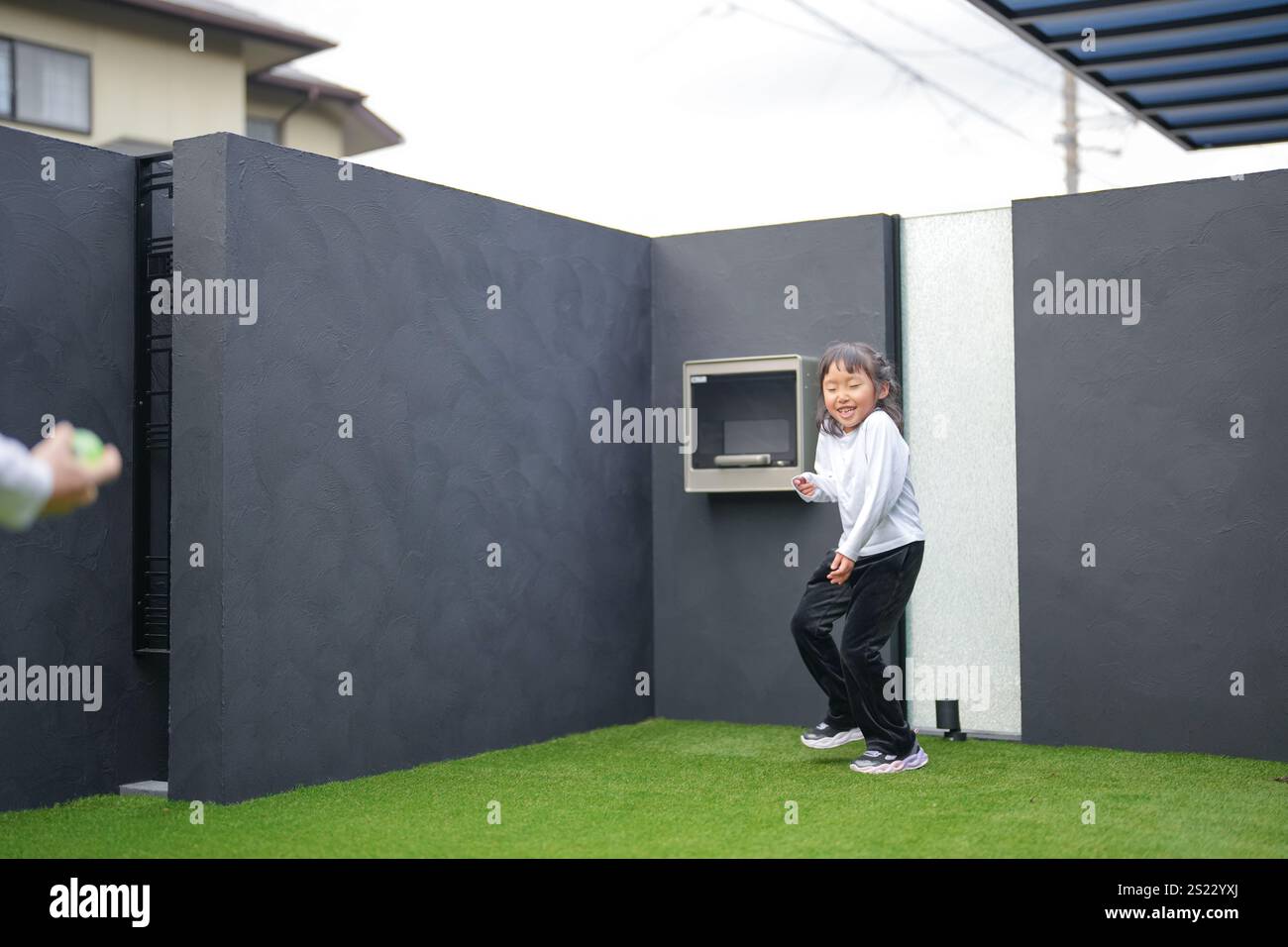 Un parent japonais et un enfant, un homme dans la vingtaine et une fille de 6 ans, jouent en se jetant des balles en plastique vert l'un sur l'autre dans le jardin clôturé de Banque D'Images