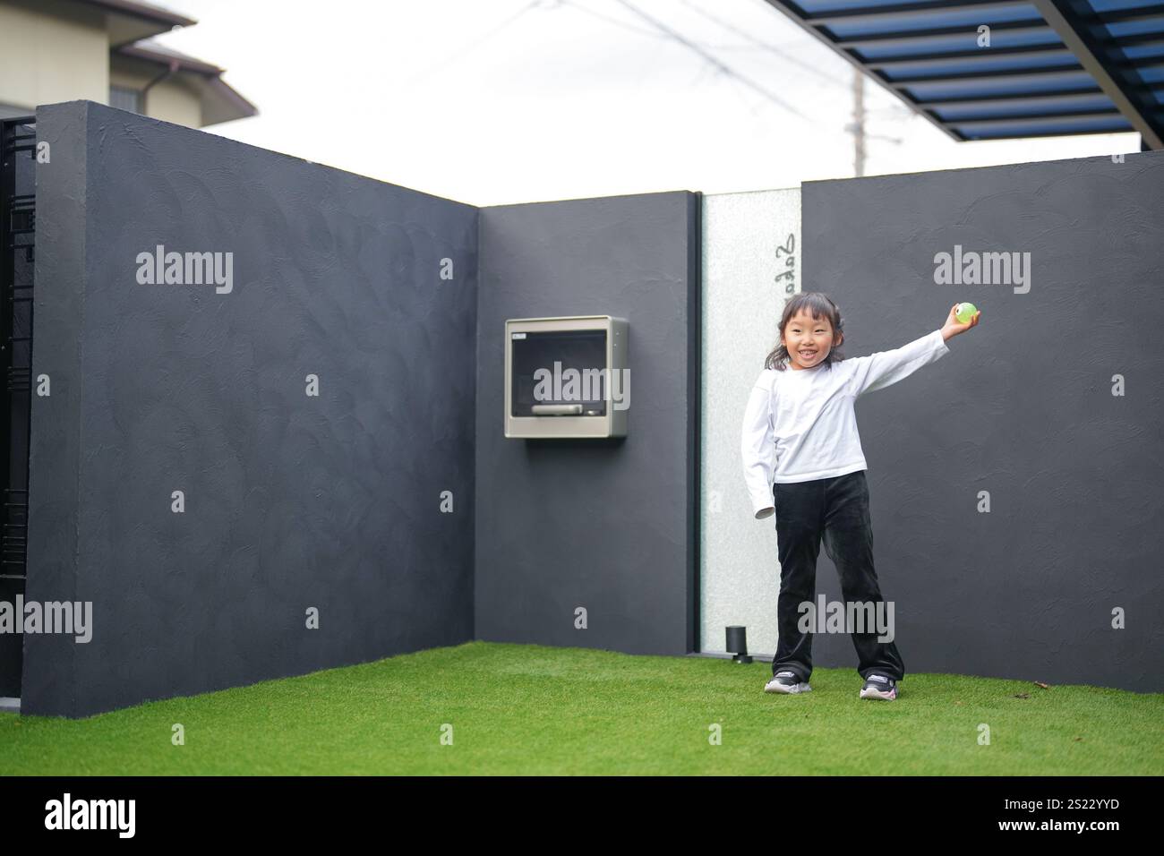 Un parent japonais et un enfant, un homme dans la vingtaine et une fille de 6 ans, jouent en se jetant des balles en plastique vert l'un sur l'autre dans le jardin clôturé de Banque D'Images