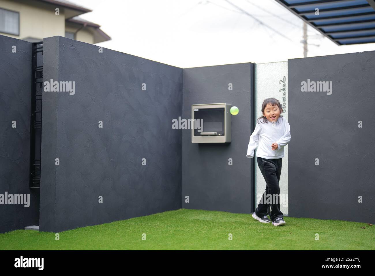 Un parent japonais et un enfant, un homme dans la vingtaine et une fille de 6 ans, jouent en se jetant des balles en plastique vert l'un sur l'autre dans le jardin clôturé de Banque D'Images