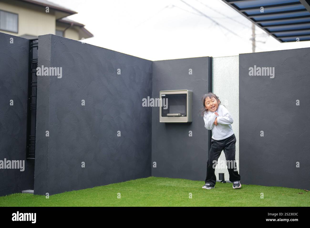 Un parent japonais et un enfant, un homme dans la vingtaine et une fille de 6 ans, jouent en se jetant des balles en plastique vert l'un sur l'autre dans le jardin clôturé de Banque D'Images