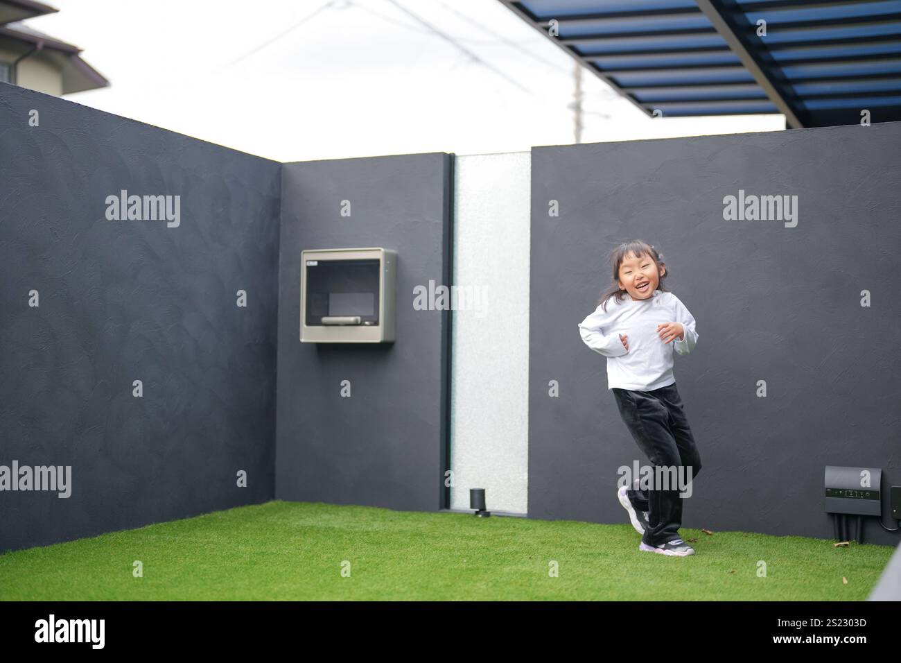 Un parent japonais et un enfant, un homme dans la vingtaine et une fille de 6 ans, jouent en se jetant des balles en plastique vert l'un sur l'autre dans le jardin clôturé de Banque D'Images