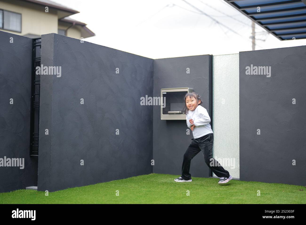 Un parent japonais et un enfant, un homme dans la vingtaine et une fille de 6 ans, jouent en se jetant des balles en plastique vert l'un sur l'autre dans le jardin clôturé de Banque D'Images