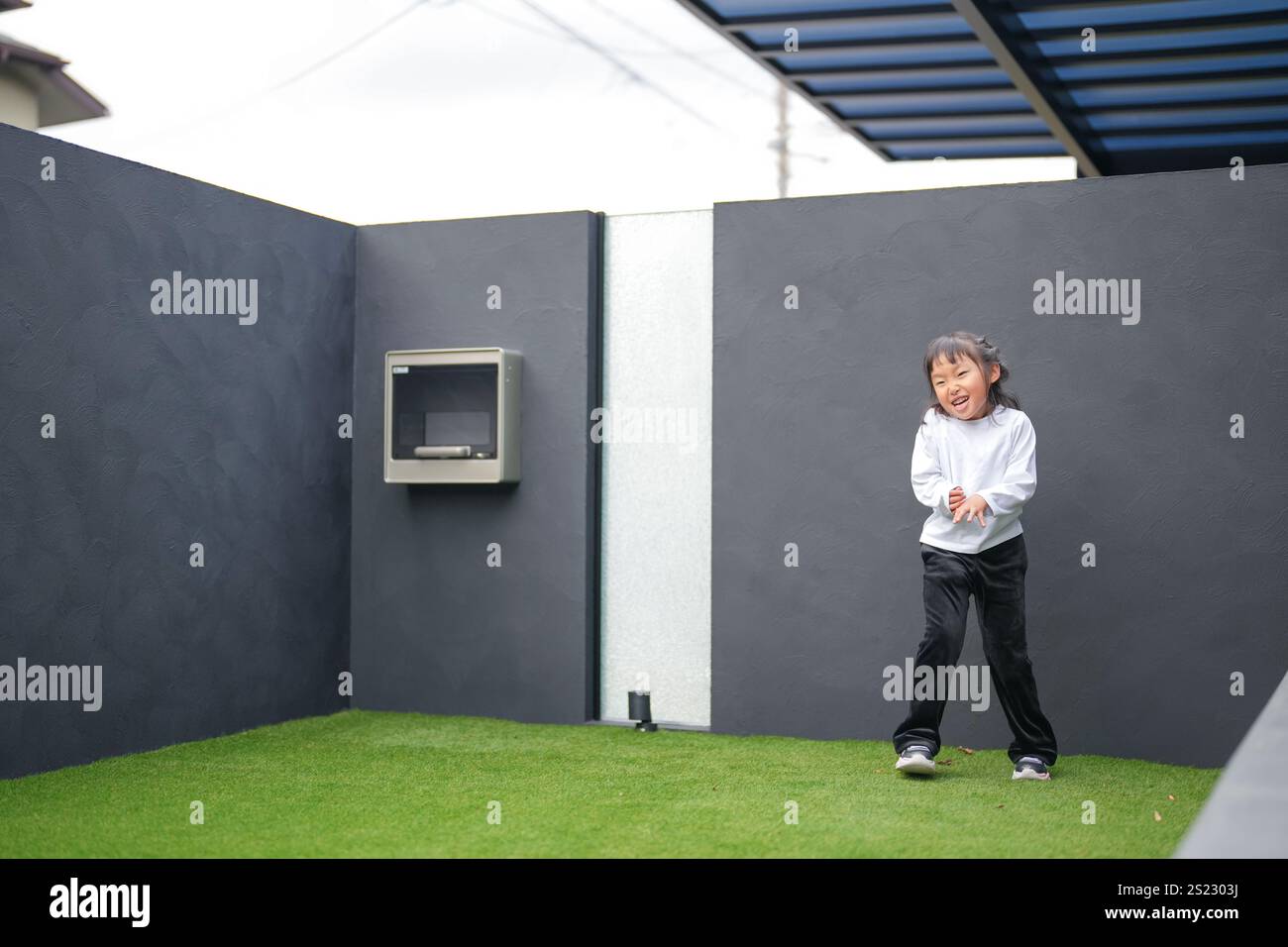 Un parent japonais et un enfant, un homme dans la vingtaine et une fille de 6 ans, jouent en se jetant des balles en plastique vert l'un sur l'autre dans le jardin clôturé de Banque D'Images