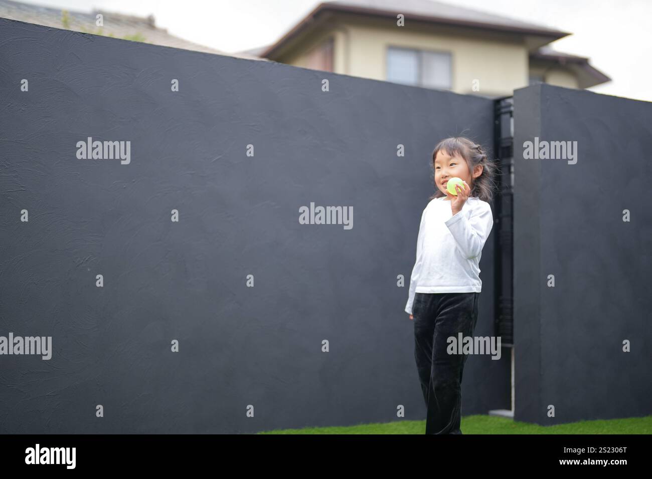 Un parent japonais et un enfant, un homme dans la vingtaine et une fille de 6 ans, jouent en se jetant des balles en plastique vert l'un sur l'autre dans le jardin clôturé de Banque D'Images