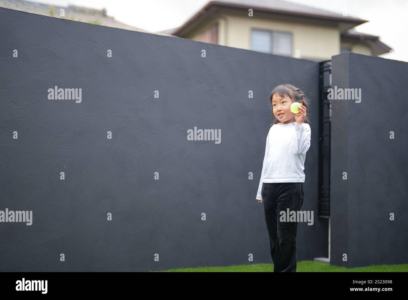 Un parent japonais et un enfant, un homme dans la vingtaine et une fille de 6 ans, jouent en se jetant des balles en plastique vert l'un sur l'autre dans le jardin clôturé de Banque D'Images