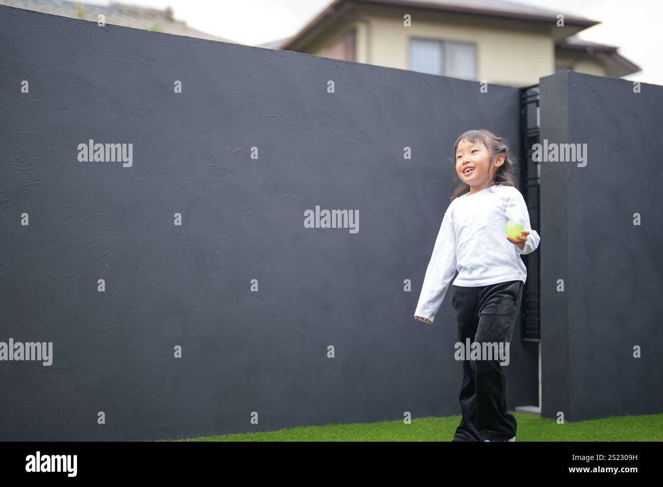 Un parent japonais et un enfant, un homme dans la vingtaine et une fille de 6 ans, jouent en se jetant des balles en plastique vert l'un sur l'autre dans le jardin clôturé de Banque D'Images