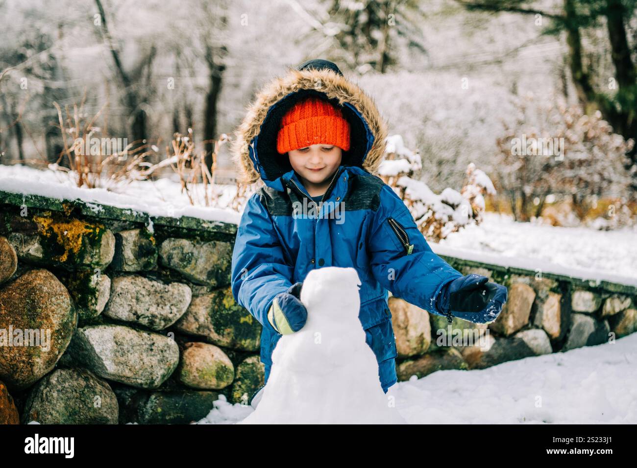 Enfant souriant façonnant bonhomme de neige à l'extérieur Banque D'Images