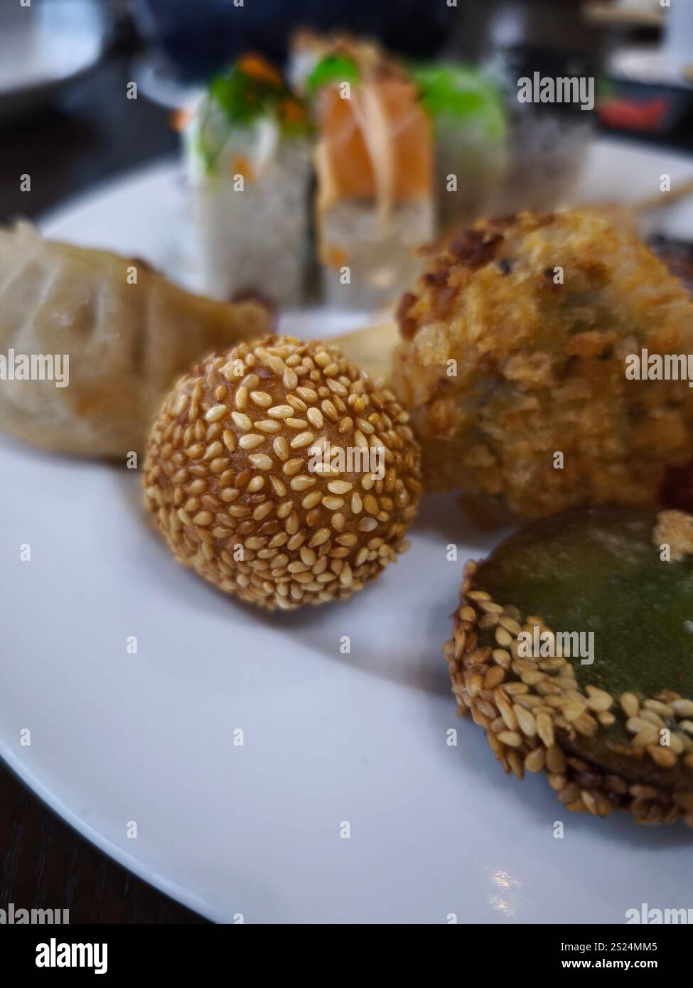 Les boules de sésame, les boulettes et les sushis partagent une assiette, mettant en valeur une expérience culinaire variée à volonté Banque D'Images
