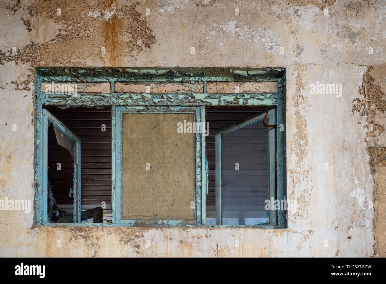 Gros plan d'une fenêtre détériorée et écaillée dans un bâtiment abandonné, avec de la peinture fissurée et une texture rustique dégradée. Banque D'Images