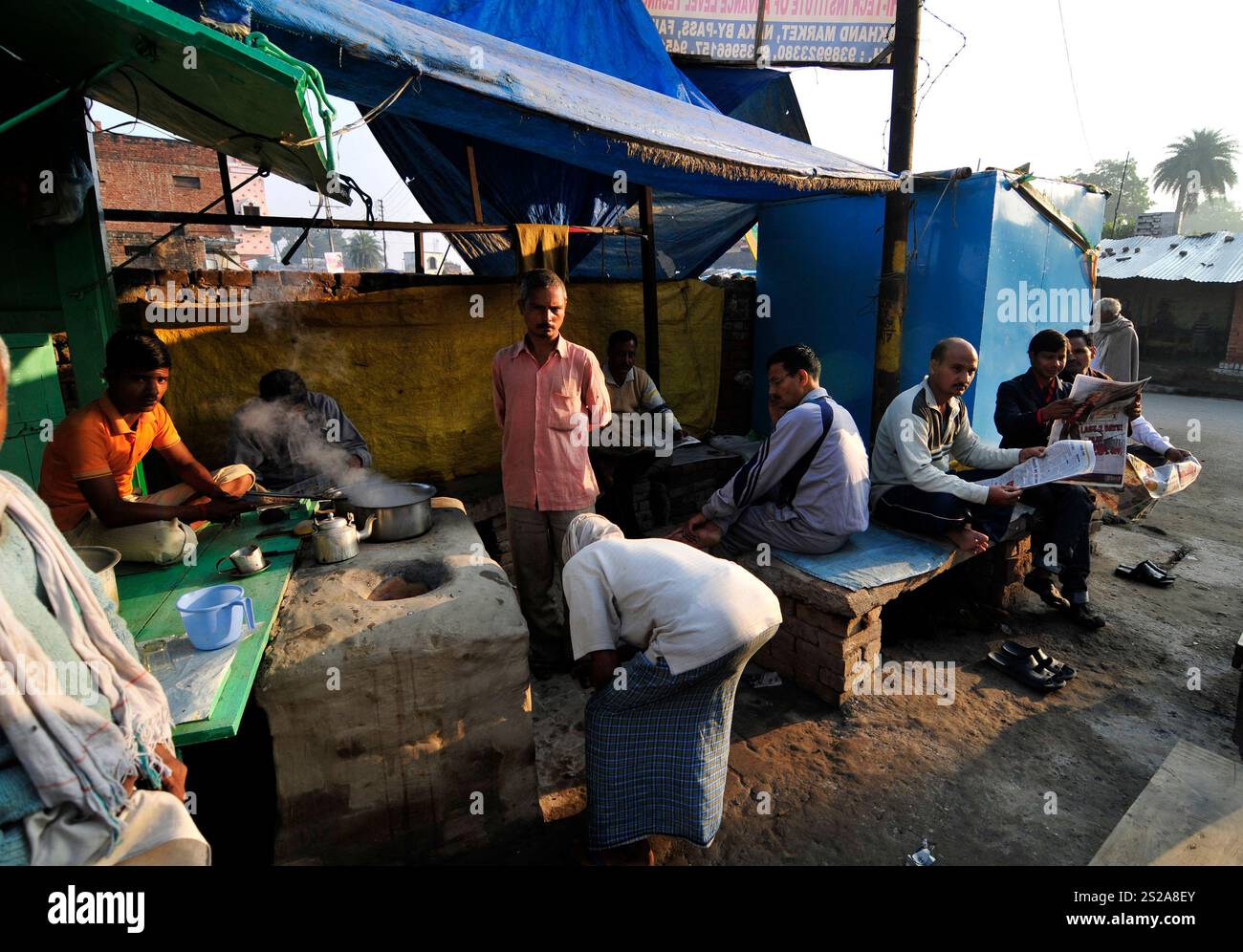 Les hommes locaux dégustant une tasse de chai chaud dans un petit magasin de thé tout en lisant le journal du matin à Ayodhya, Uttar Pradesh, Inde. Banque D'Images