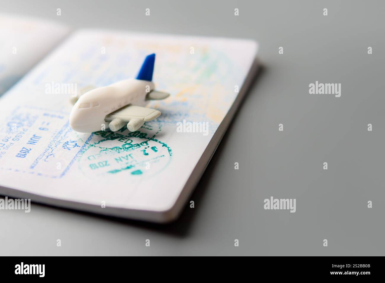 Un passeport avec plusieurs timbres est ouvert sur une surface grise avec un avion jouet. Copier l'espace pour le texte. Concept de voyage, d'exploration et d'aventure. Banque D'Images