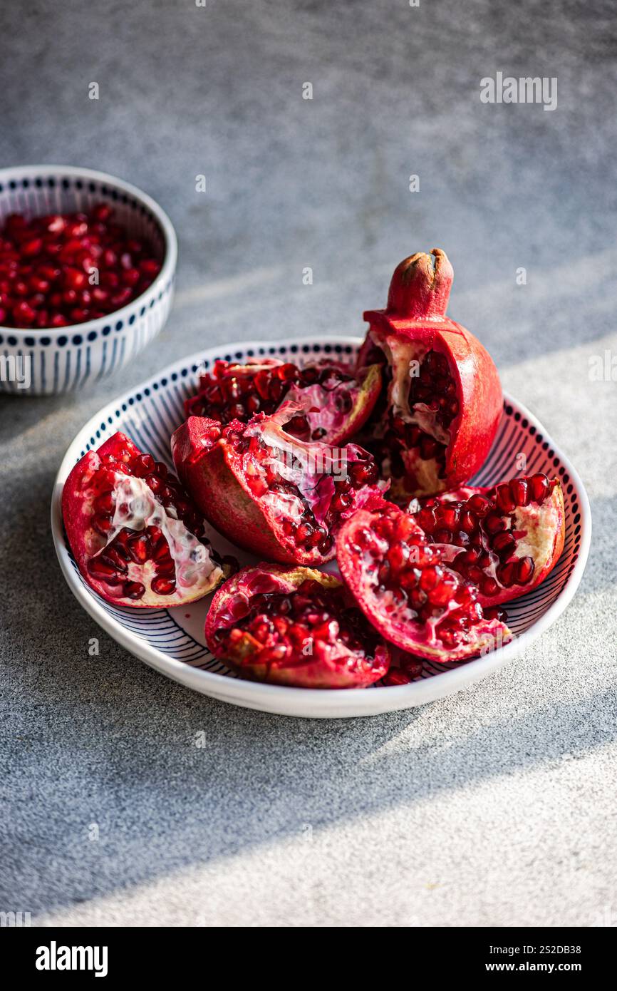Gros plan d'un plat de grenades fraîches ouvertes sur une table avec un bol de graines de grenade Banque D'Images