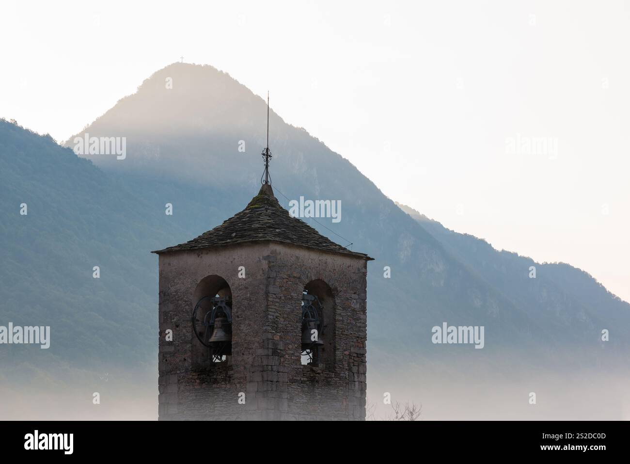 Le clocher roman émerge du brouillard avec des montagnes en arrière-plan et le soleil sur le point de se lever Banque D'Images