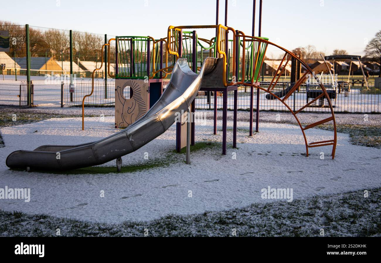 Terrain de jeux enneigé avec toboggan et cadre d'escalade en hiver matin, vide d'enfants, entouré d'une clôture de parc Banque D'Images