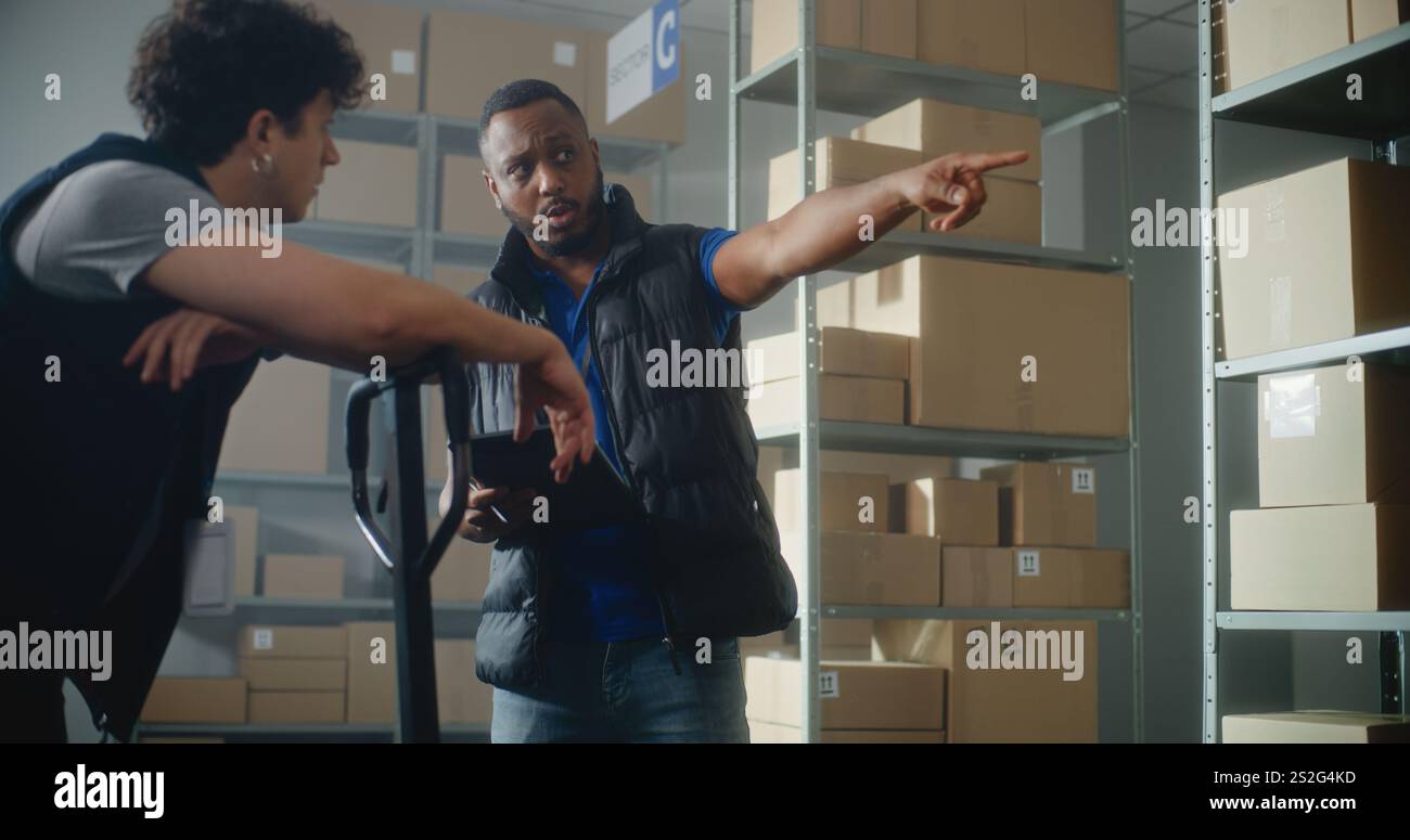 Employés d'entrepôt multiethnique travaillant dans le centre de tri du service de livraison ou boutique en ligne : le coordinateur logistique afro-américain utilise une tablette, parle à des collègues, donne des instructions. Banque D'Images