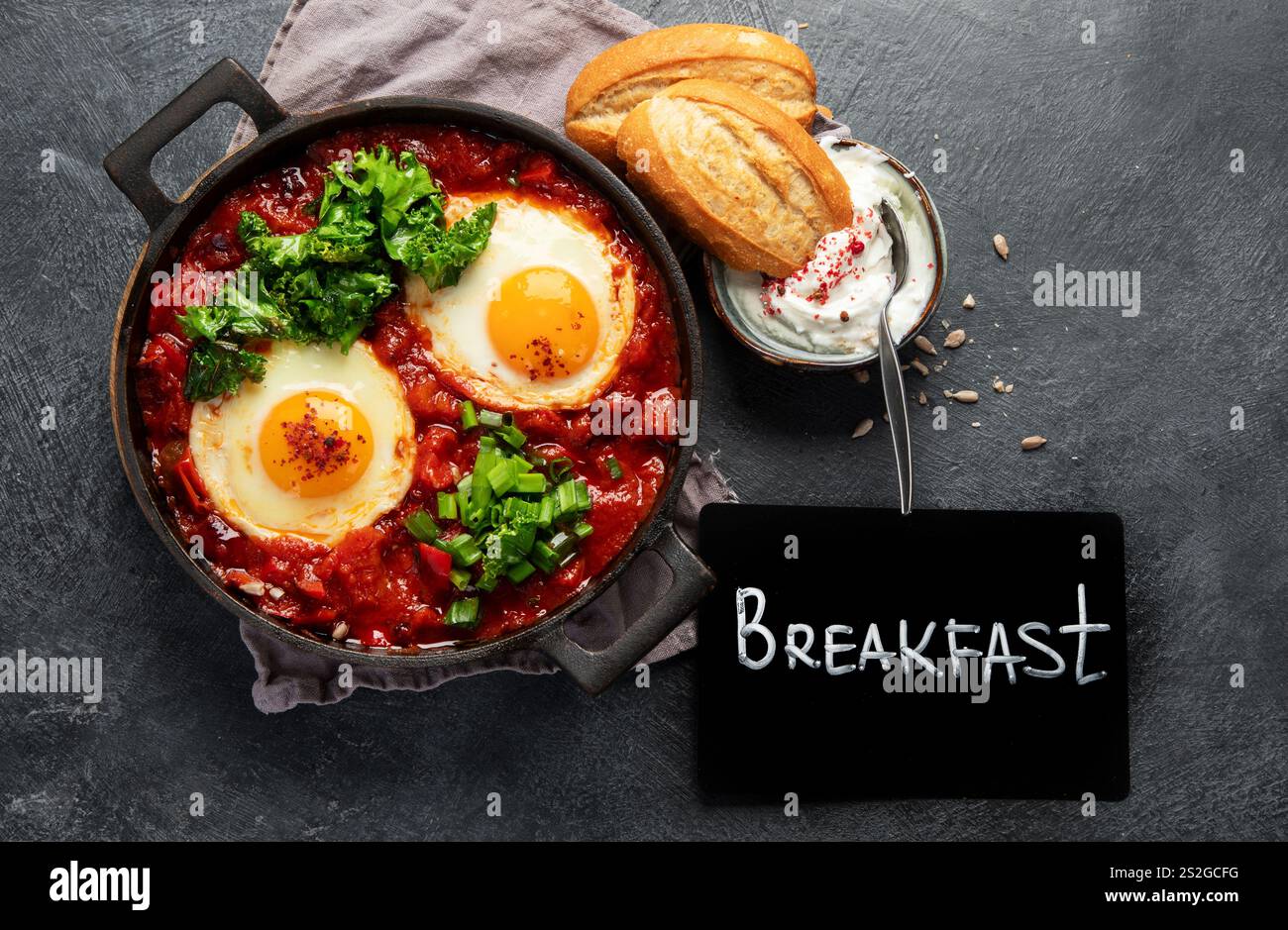 Oeufs Shakshuka dans une casserole avec du pain sur un fond sombre. Oeufs pochés dans une sauce épicée au poivre tomate. Œufs brouillés juifs traditionnels. Vue de dessus. Banque D'Images