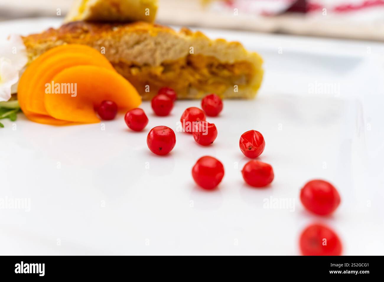Une tranche de gâteau se trouve sur une assiette blanche, entourée de baies rouges vives et de tranches de fruits orange, créant une présentation colorée et invitante parfaite Banque D'Images