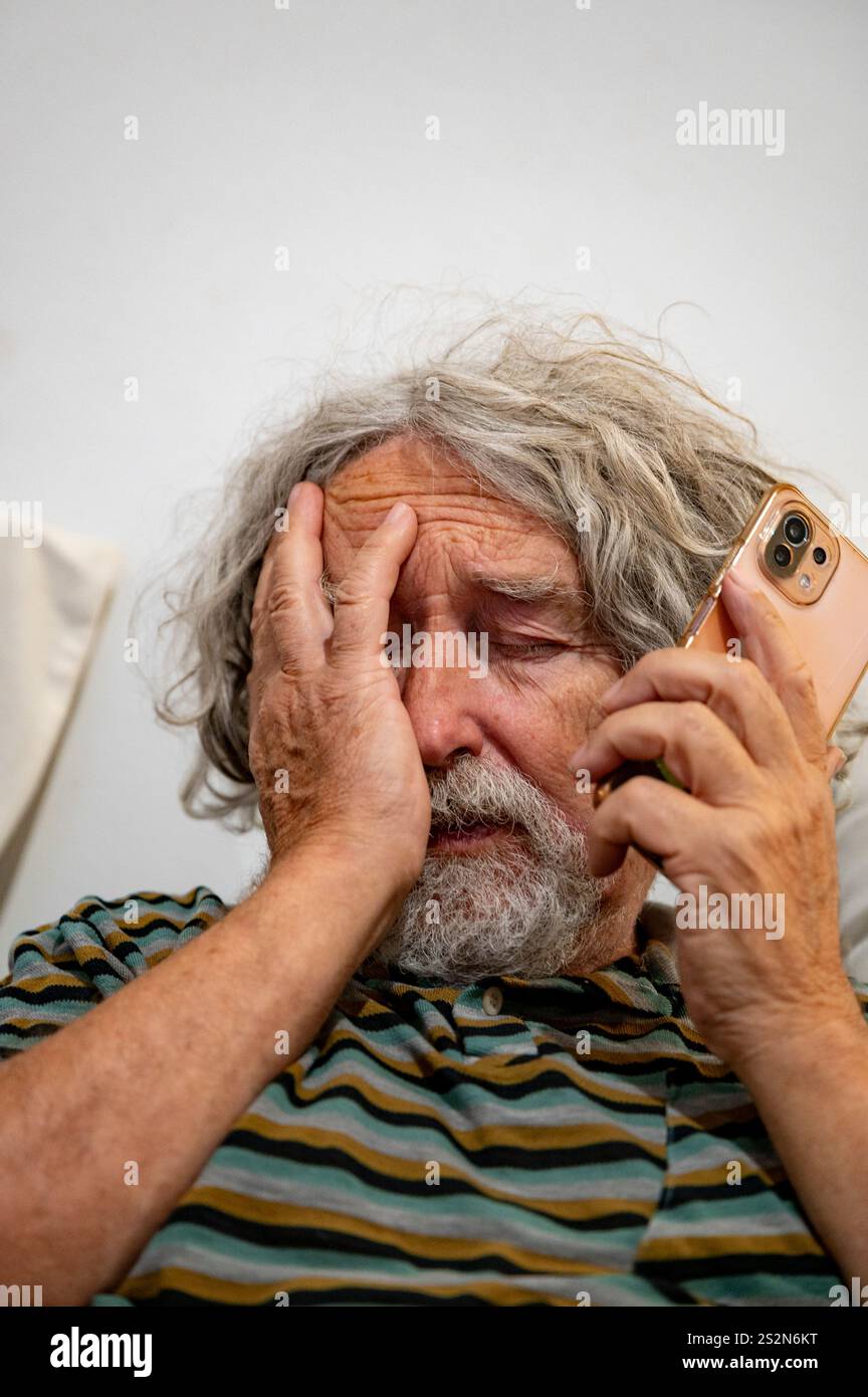 Un homme âgé en détresse, tenant sa tête d'une main tout en parlant au téléphone, véhiculant inquiétude ou frustration. Banque D'Images