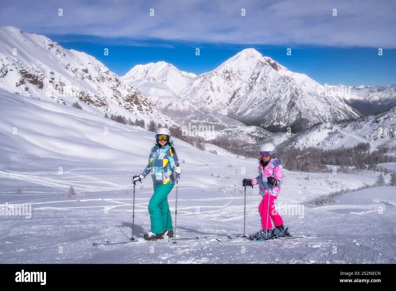 Deux skieurs naviguent à travers la neige poudreuse intacte, mettant en valeur leurs tenues vibrantes et colorées dans le cadre majestueux et époustouflant des montagnes imposantes, Montgenevre, Alpes, France Banque D'Images