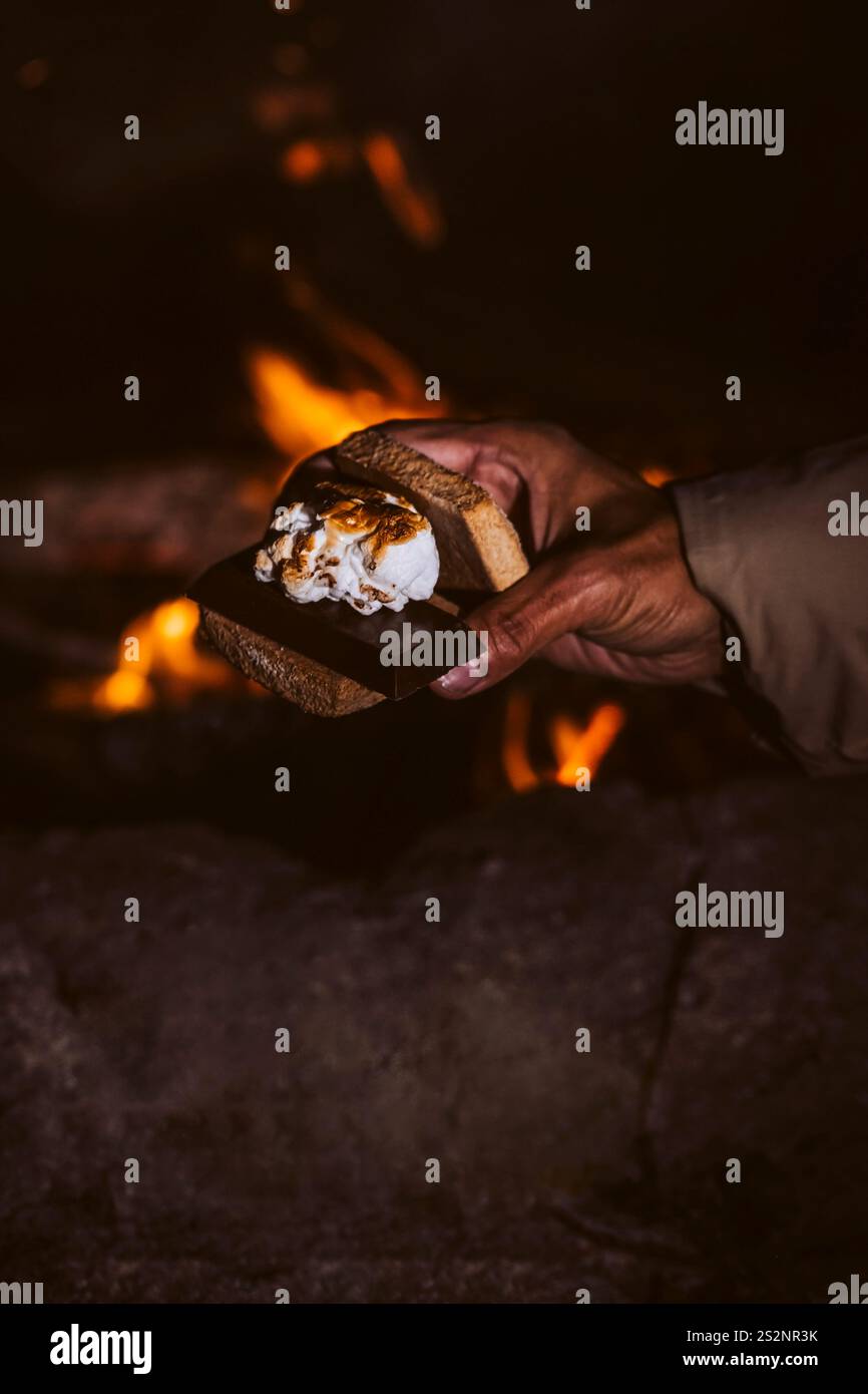 Main d'homme tenant un sandwich s'More avec un foyer en arrière-plan Banque D'Images