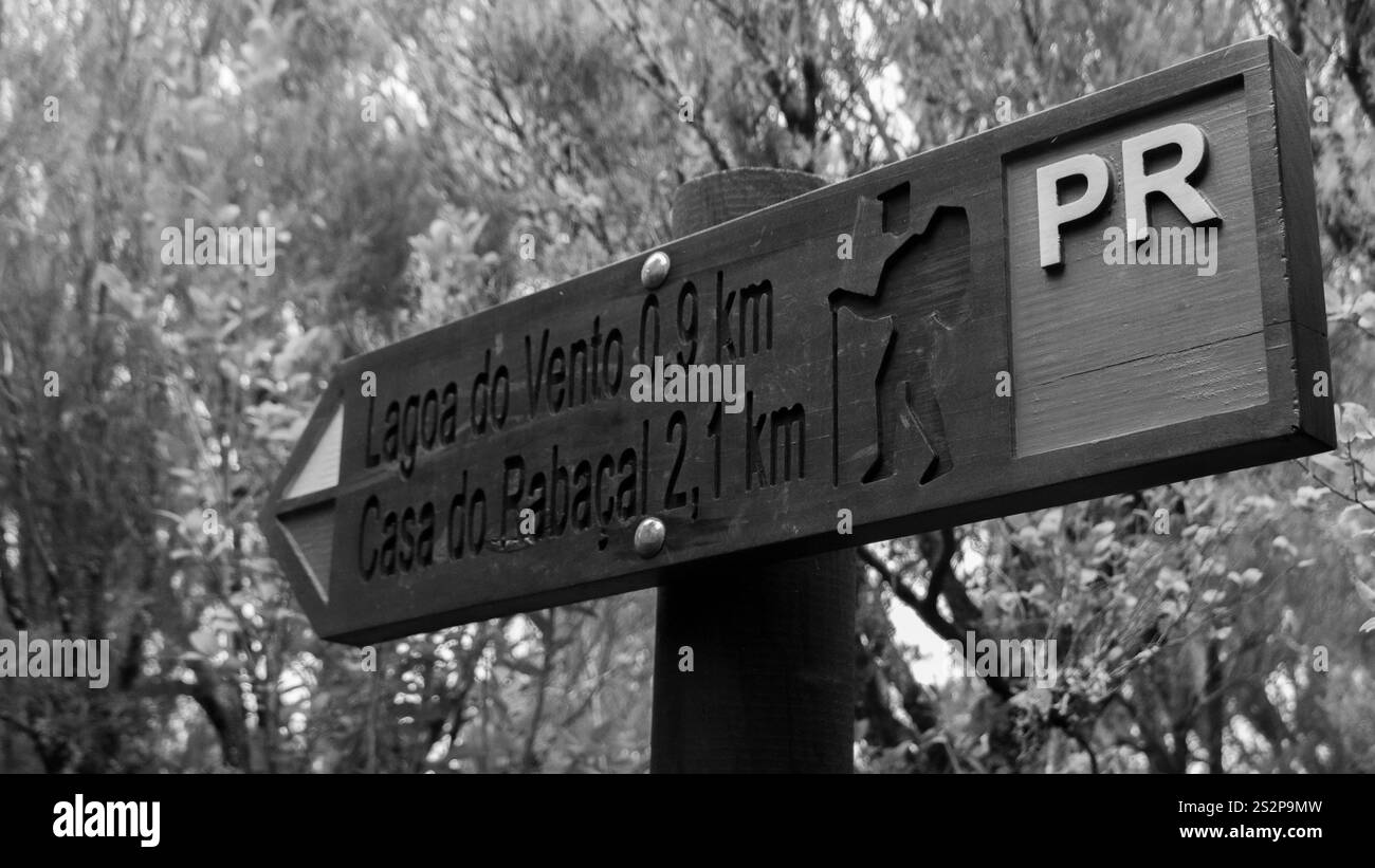 Une photographie en noir et blanc d'un panneau de sentier de randonnée en bois pointant vers Lagoa do Vento et Casa do Rabaçal. Le signe rustique se fond dans le naturel pour Banque D'Images