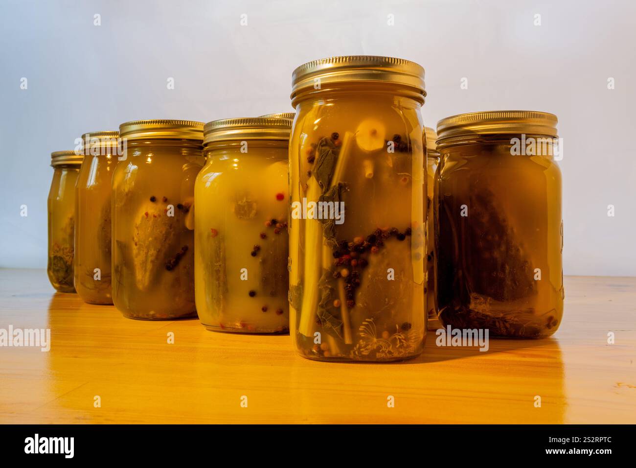Bocaux en verre remplis de concombres marinés sur une table en bois sur un fond blanc. Banque D'Images
