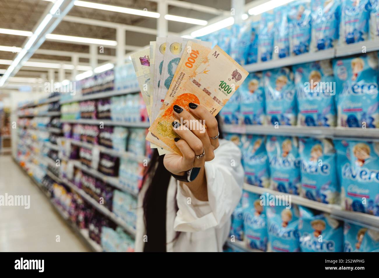 Jeune femme tenant de l'argent - Pesos argentins - dans le supermarché. Économie Argentine. Concept d'inflation, dévaluation de la monnaie Argentine Banque D'Images
