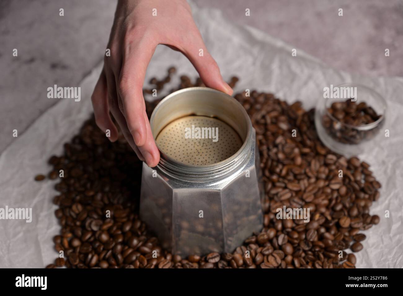 La main de la femme se prépare à faire du café dans une machine à café geyser moka. Grains de café aromatiques frais éparpillés autour. Arrière-plan clair Banque D'Images