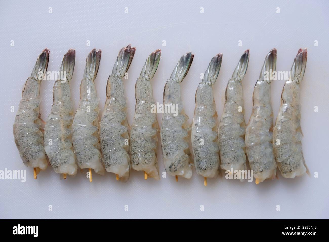 Gros plan de crevettes fraîches pelées non cuites sur une planche à découper blanche. Banque D'Images
