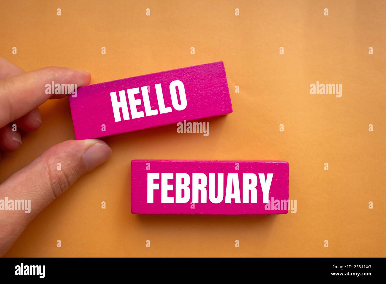 Bonjour février message écrit sur des blocs de bois rose avec fond orange. Symbole conceptuel bonjour février. Copier l'espace. Banque D'Images