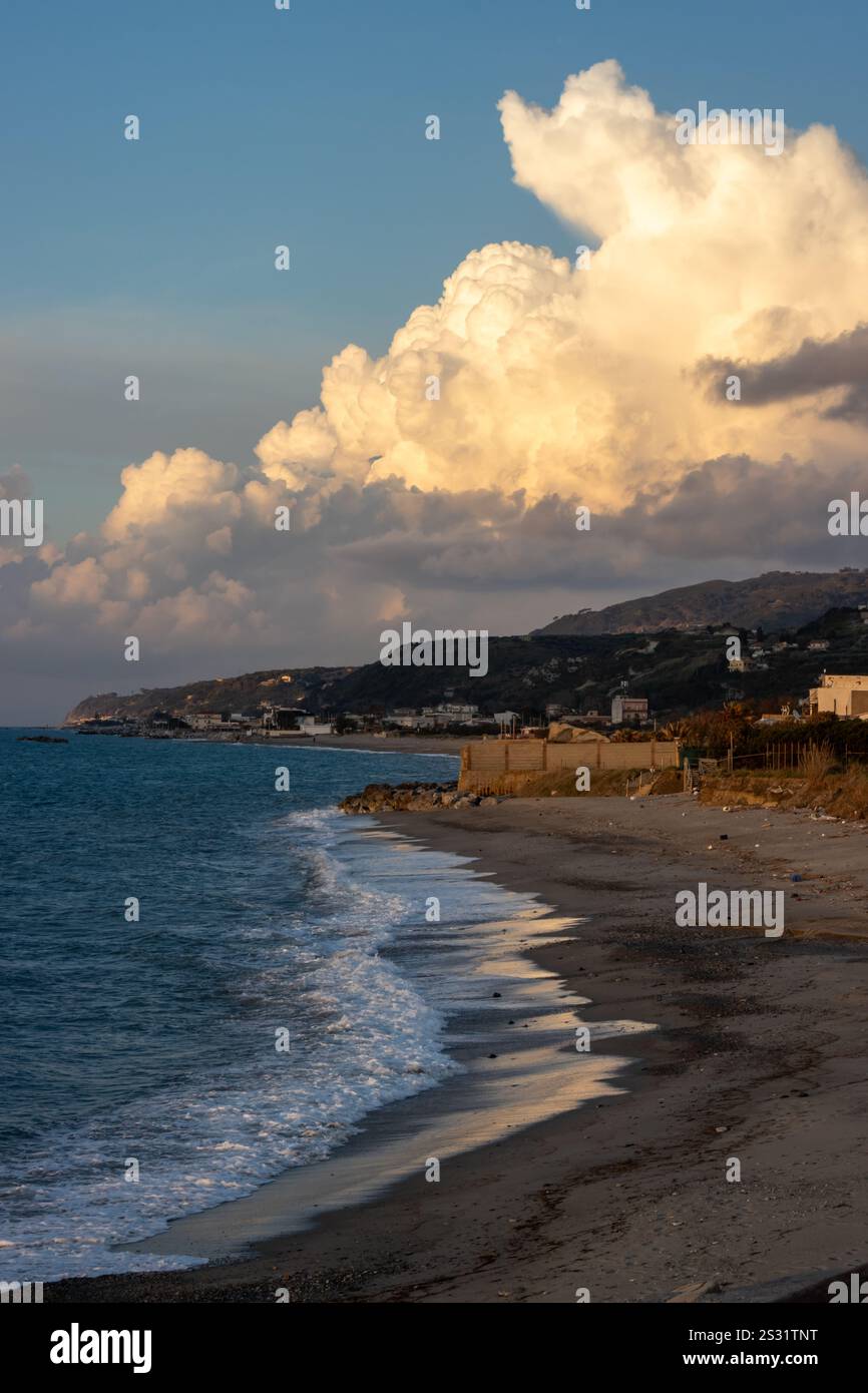 Soirée à la plage de sable au moment du coucher du soleil. Calme mer Tyrrhénienne (Méditerranée). Nuage lumineux enligé par la lumière du soleil. Torregrotta, Sicile, I. Banque D'Images