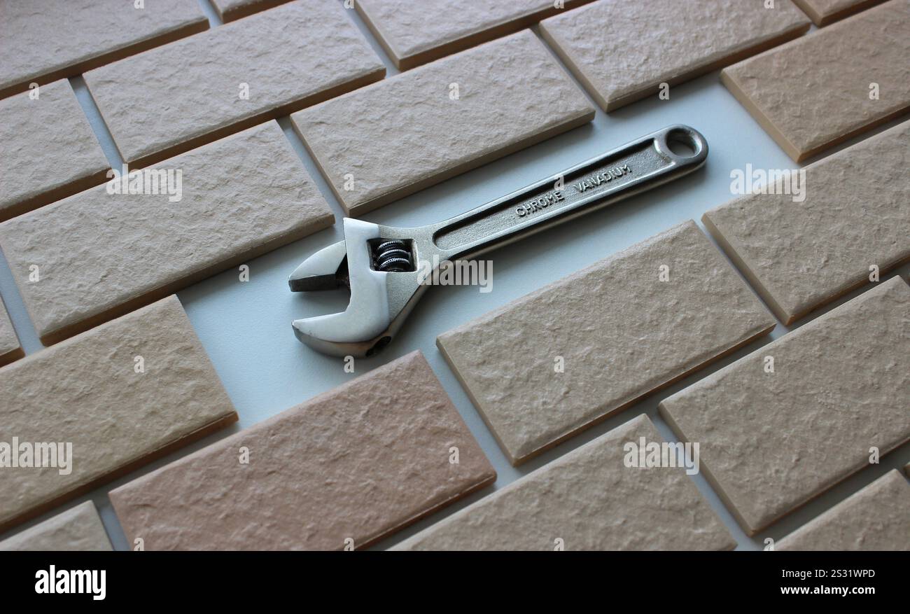 Une clé réglable à la place d'un carreau manquant sur une surface entièrement carrelée. Mâchoires ouvertes de la clé réglable chromée sur l'espace libre dans la surface couverte br Banque D'Images