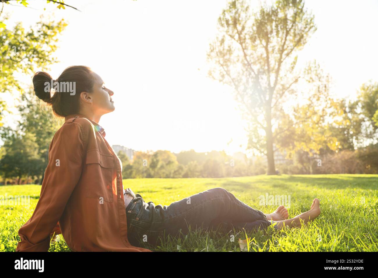 Femme urbaine assise sur l'herbe verte dans le parc de la ville se relaxant après le travail. Équilibre entre vie professionnelle et vie privée, santé mentale et rétablissement. Banque D'Images