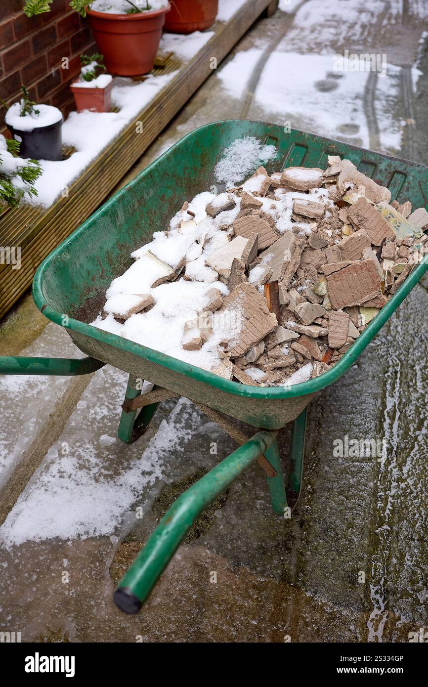 Brouette remplie de briques enneigées et de ciment dans un jardin d'hiver. Banque D'Images