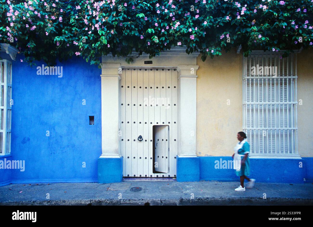 Une travailleuse domestique racialisée passe devant un bâtiment colonial à Carthagène, en Colombie, soulignant le contraste entre charme historique et inégalité sociale. Banque D'Images