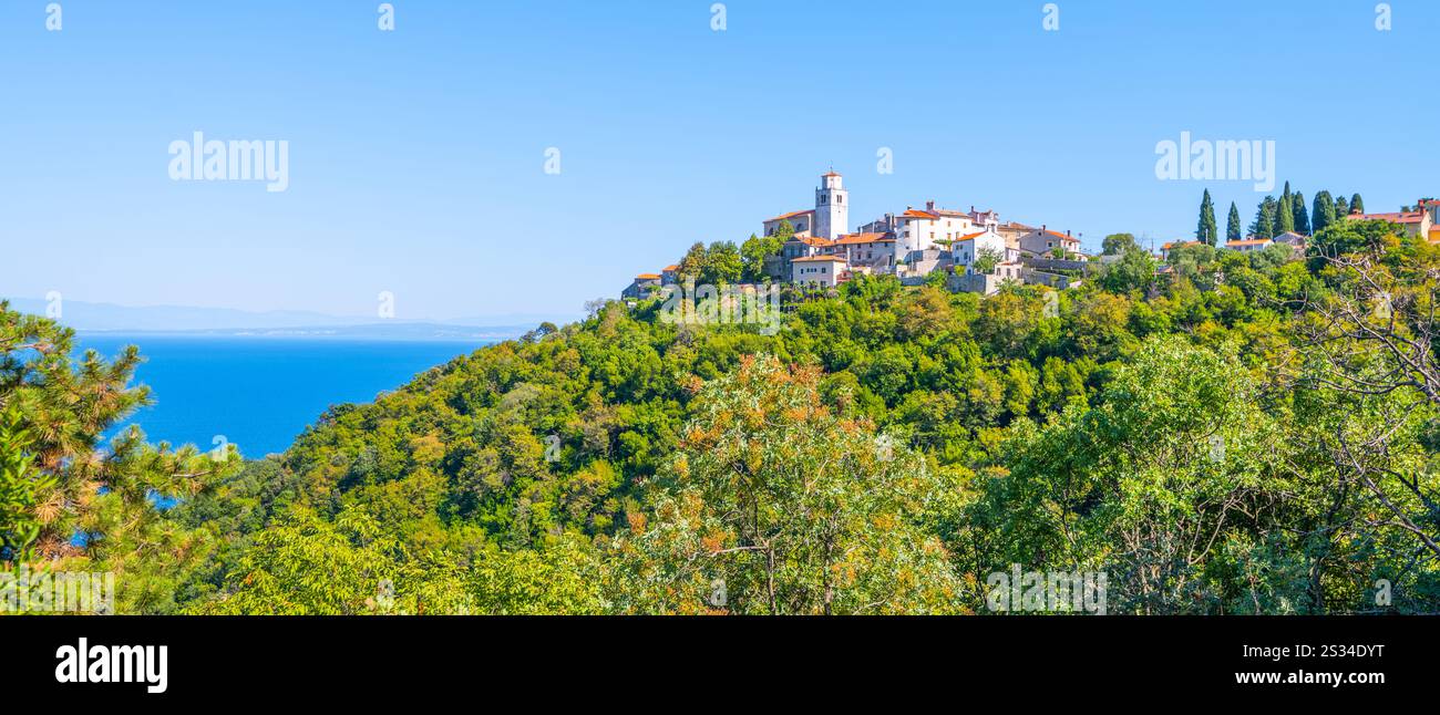 Une végétation luxuriante entoure un charmant village perché sur une colline surplombant la mer Adriatique le long de la péninsule d'Istrie. Le beau temps rehausse le paysage côtier pittoresque. Banque D'Images