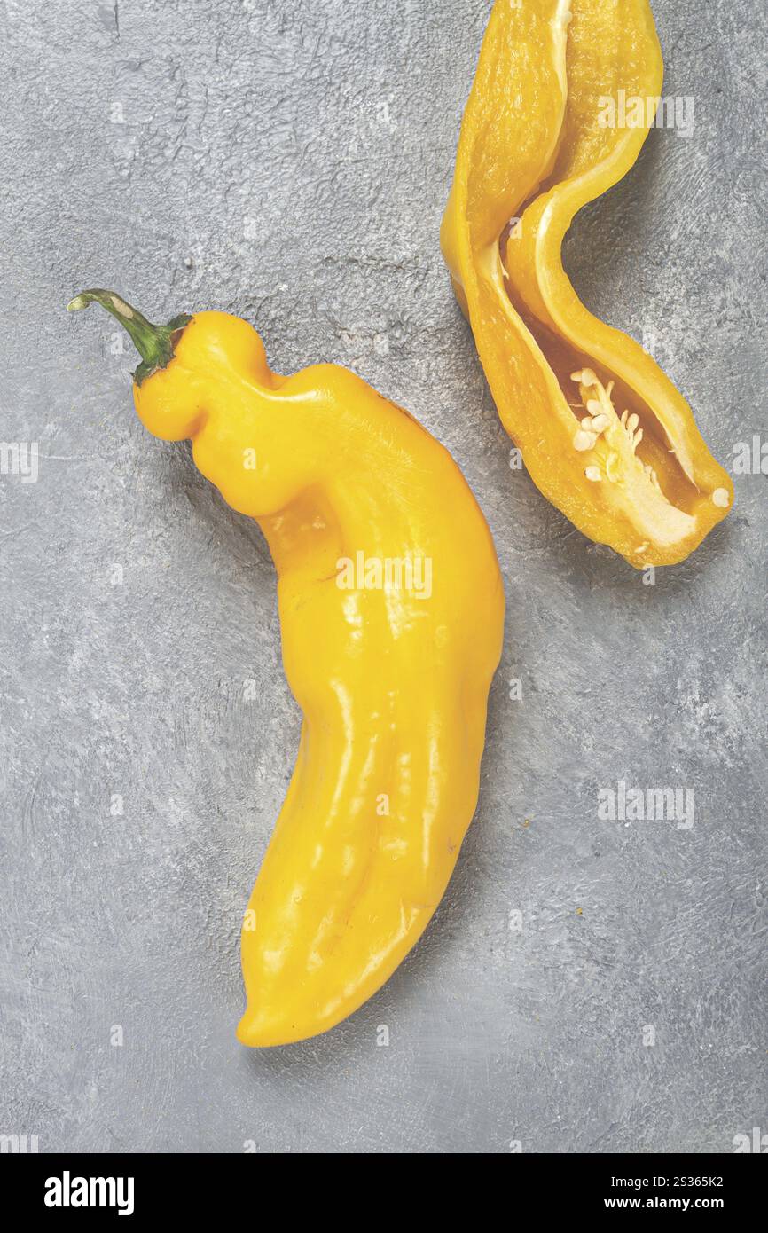 Les piments jaunes vifs sont disposés sur une surface grise, présentant un poivre entier à côté d'un autre qui est coupé en tranches ouvertes, exposant des graines vibrantes Banque D'Images