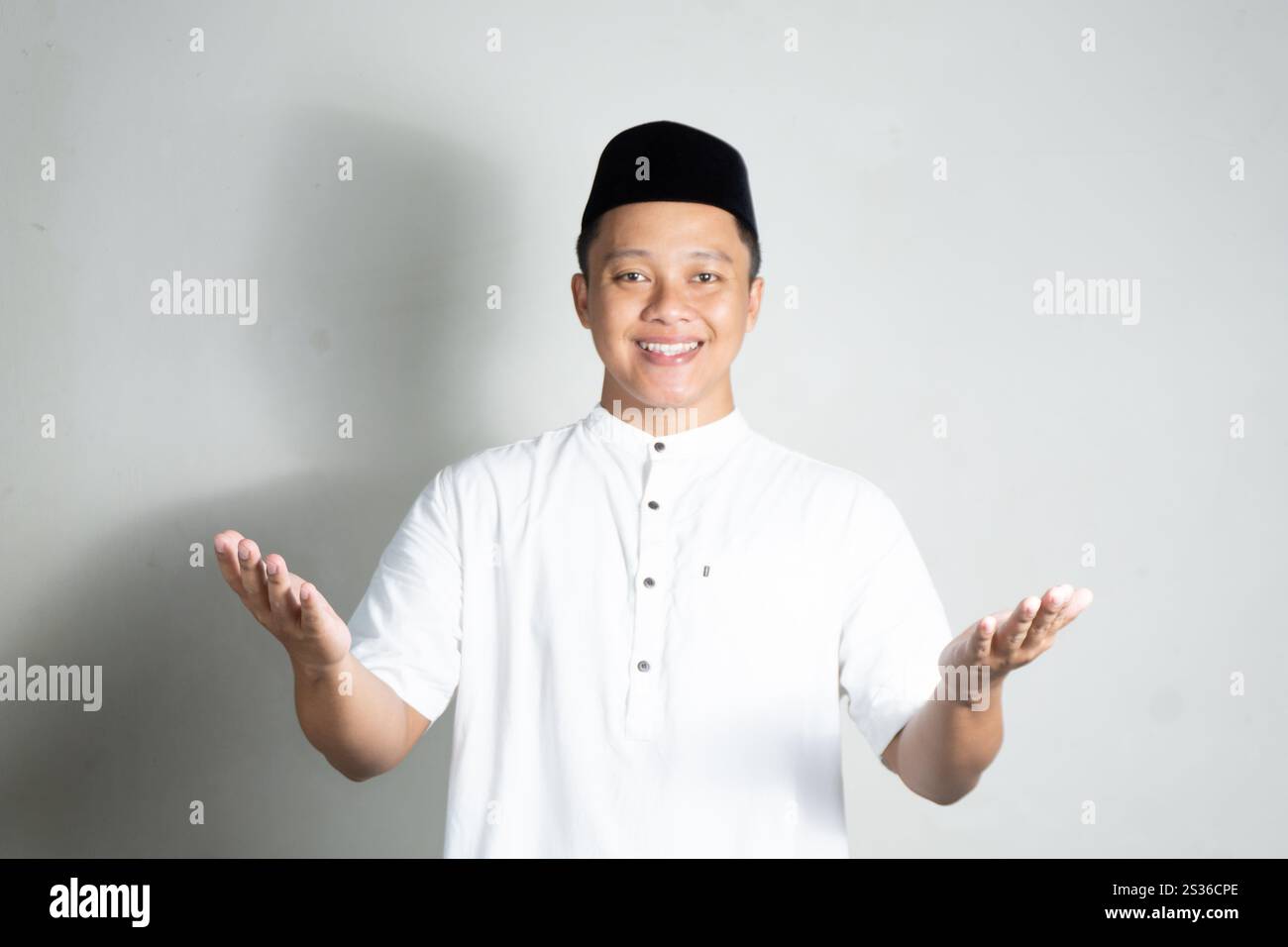 Homme asiatique musulman souriant heureux et montre la salutation de l'Aïd Moubarak et le geste de bienvenue du Ramadan sur fond blanc. Concept de personnes religieuses Banque D'Images