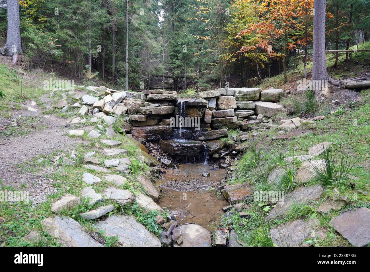 Gros plan d'une petite chute d'eau se déversant sur des rochers couverts de mousse dans le parc régional. Cascade de rivière faite à la main de petites pierres. Gros plan d'un petit Banque D'Images