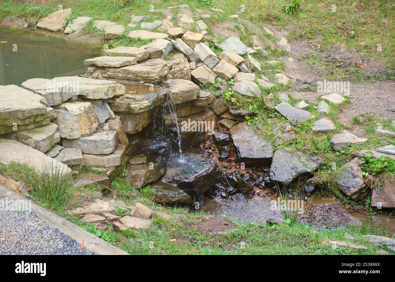 Gros plan d'une petite chute d'eau se déversant sur des rochers couverts de mousse dans le parc régional. Cascade de rivière faite à la main de petites pierres. Gros plan d'un petit Banque D'Images