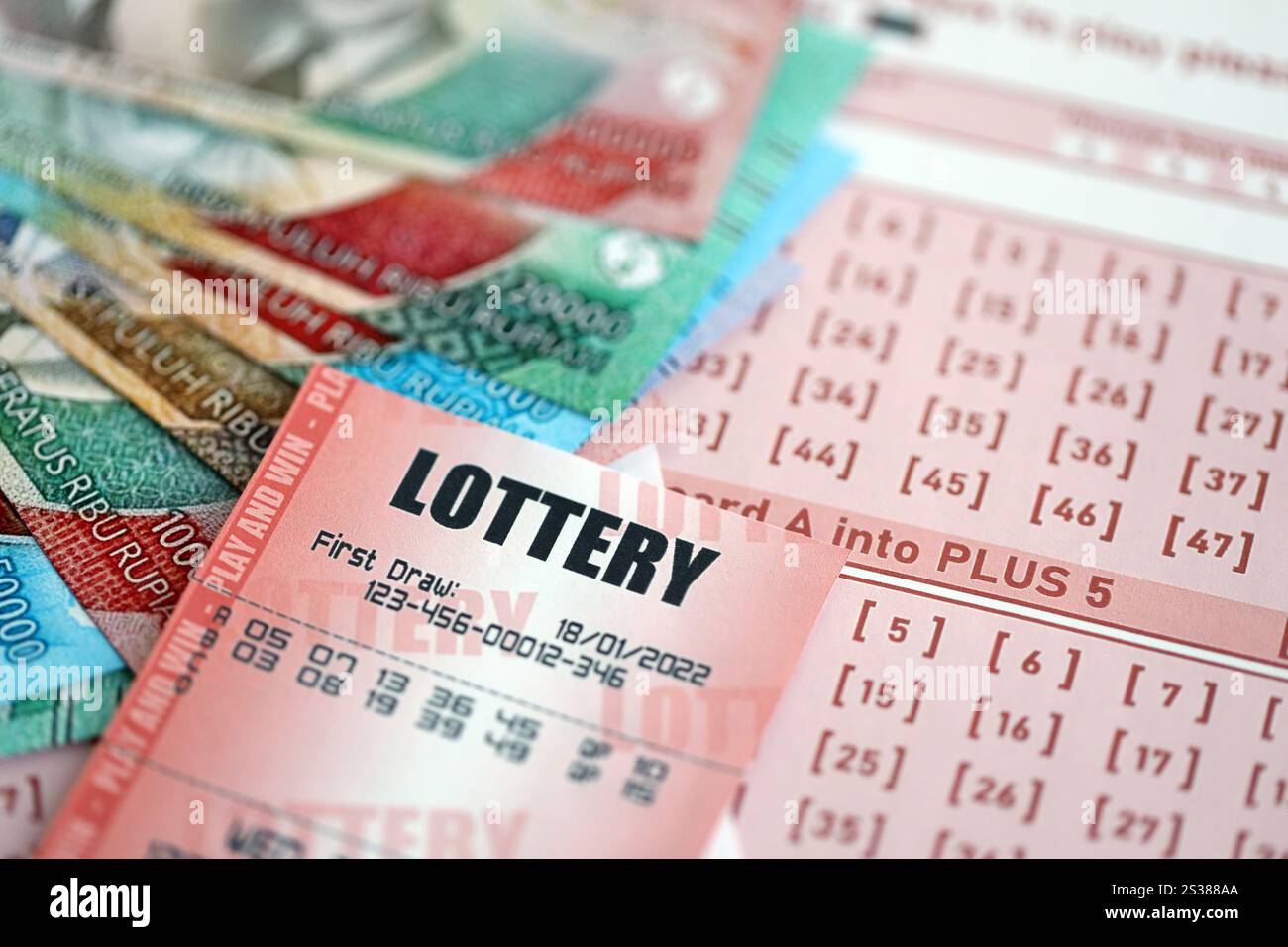 Billet de loterie rouge se trouve sur des feuilles de jeu roses avec des factures d'argent rupiah indonésiennes. Concept de jeu de loterie ou dépendance au jeu en indonésie. Rouge Banque D'Images