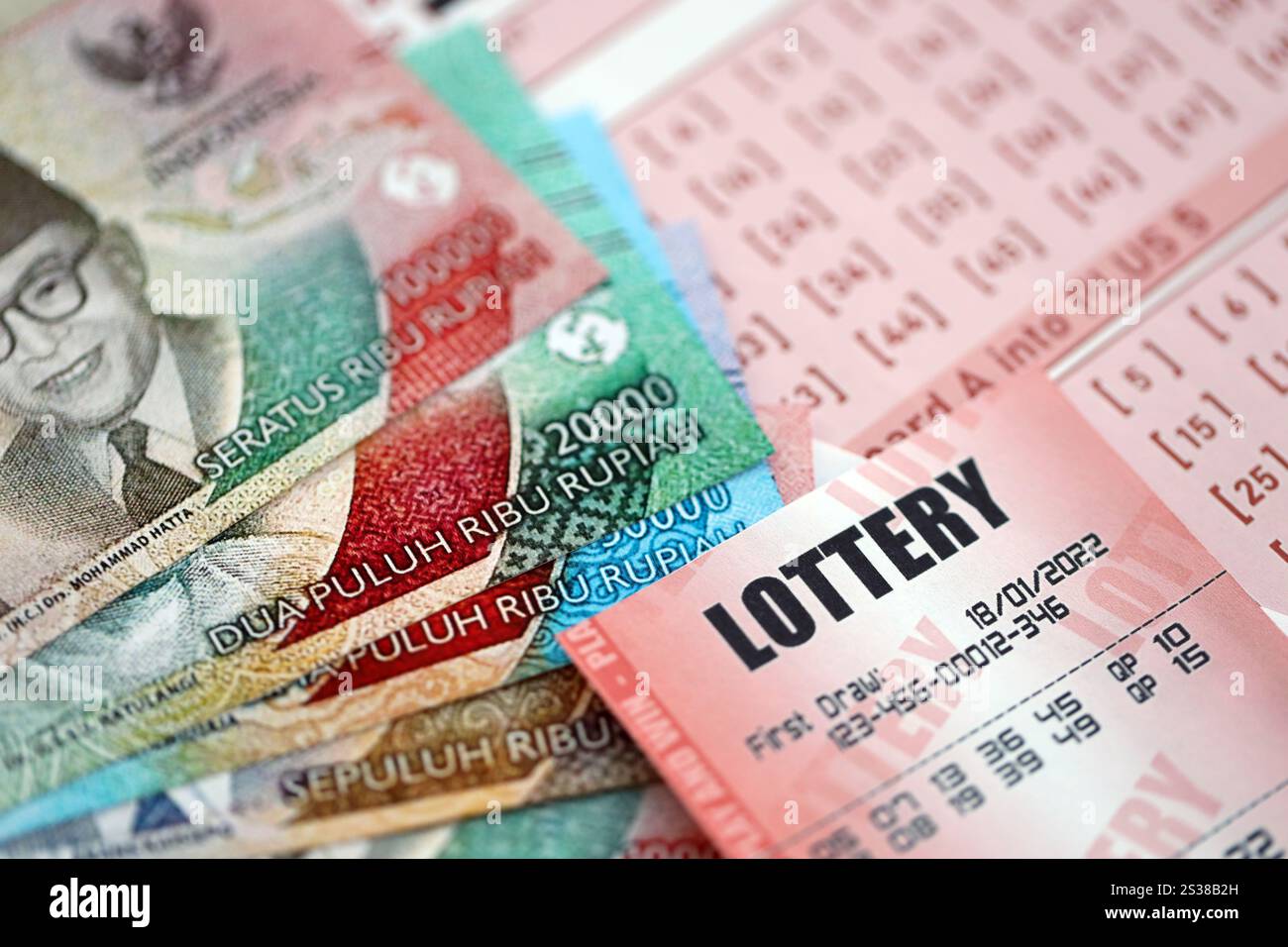 Billet de loterie rouge se trouve sur des feuilles de jeu roses avec des factures d'argent rupiah indonésiennes. Concept de jeu de loterie ou dépendance au jeu en indonésie. Rouge Banque D'Images